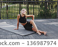 Happy preteen girl sitting on yoga mat in black sportswear outdoors in forest, smiling while looking away. Child enjoying nature, youth fitness and positive outdoor activity 136987974