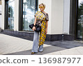 Woman with short blonde hair and yellow sunglasses wearing bold plaid top and flared jeans, standing on sidewalk. Modern fashion portrait 136987977