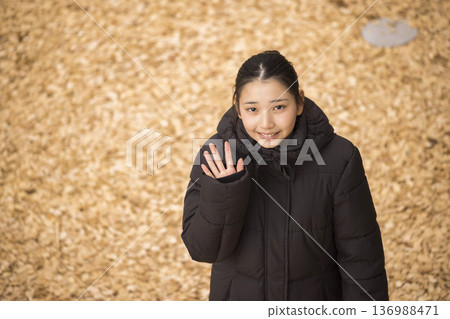 一位身著冬裝的女子站在鋪滿木屑的公園裡。 136988471