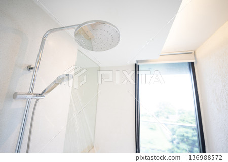 Cold Water was pouring out from a large shower in the bathroom with a glass window. 136988572