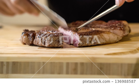 The close up image of a chef cutting medium rare grilled beef steak with chef knives on a wooden chopping board. 136988587