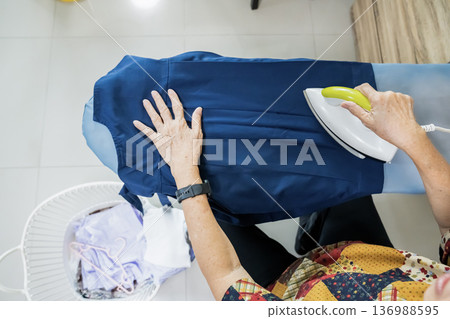 Senior citizens ironing student skirt and clothing in a house. 136988595