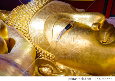 The close up face of the Reclining Buddha statue image at Wat Phra Phut Saiyat or Saiyat Buddhist temple in Phetchaburi province, Thailand. 136988662