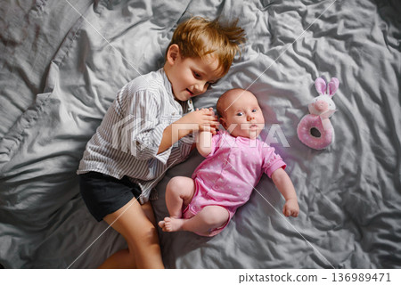 Loving Brother Holding Baby Sister On Grey Bed Loving Brother Holding Baby Sister On Grey Bed 136989471