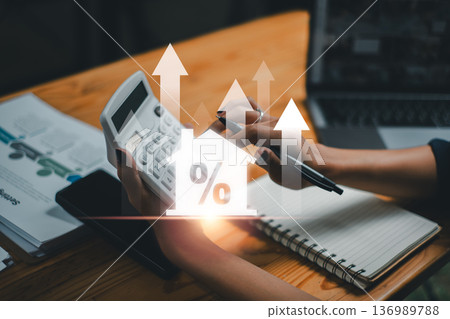 A person using a calculator with digital graphs and percentage symbols, representing financial growth and analysis in a business setting. 136989788
