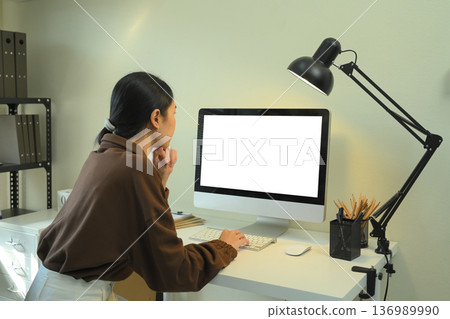 Woman working at a desktop computer in a modern office, focusing on the screen under desk Woman working at a desktop computer in a modern office, focusing on the screen under desk 136989990