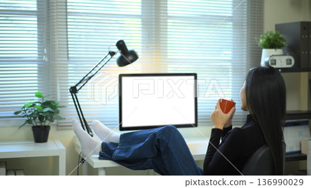 Woman relaxing with coffee at desk and empty screen computer in modern office Woman relaxing with coffee at desk and empty screen computer in modern office 136990029