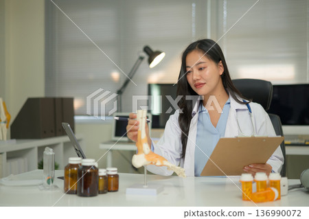 Doctor studying a bone model at a desk, showing medical learning, anatomy education, and professional training 136990072