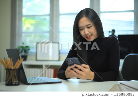 Woman using smartphone at desk in modern office workspace 136990092
