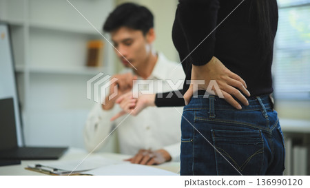 Close-up of a tense office moment where a woman stands with hands on hips while a coworker gestures at documents Close-up of a tense office moment where a woman stands with hands on hips while a coworker gestures at documents 136990120