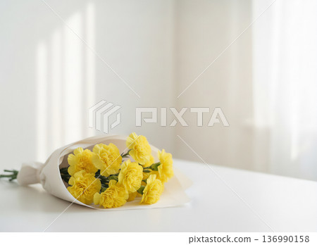 陽光灑進一間白色房間,桌上擺放著一束黃色康乃馨。 陽光灑進一間白色房間,桌上擺放著一束黃色康乃馨。 136990158