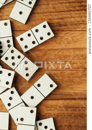 Players enjoy a game with white dominoes on a wooden table in the afternoon light 136990707
