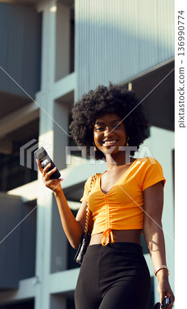 Woman walks outside with phone in hand in urban area during daytime 136990774