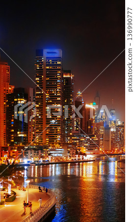 City skyline lights up the night along the river with buildings in Dubai, UAE near water 136990777