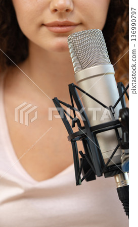 Woman speaks into microphone while recording audio in studio setting during daytime hours 136990797