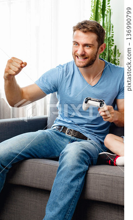 Man plays video game with child on couch during afternoon at home in living room Man plays video game with child on couch during afternoon at home in living room 136990799