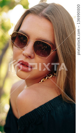 Woman in sunglasses poses outdoors with natural light on her face during sunny afternoon 136990800