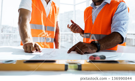 Two construction workers discuss plans in an office with bright sunlight during the day 136990844