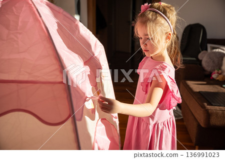 Young child playing with pink tent indoors during daylight hours Young child playing with pink tent indoors during daylight hours 136991023