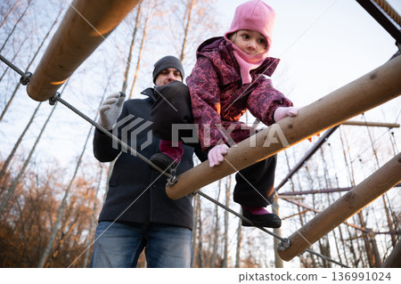 Child climbs on playground equipment while adult supervises in a park during evening hours Child climbs on playground equipment while adult supervises in a park during evening hours 136991024