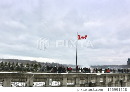 Niagara Falls in winter and the Canadian flag. View of the observation area where tourists gather. Niagara Falls in winter and the Canadian flag. View of the observation area where tourists gather. 136991328