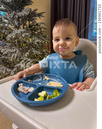 Messy toddler eating in high chair by christmas tree 136991710