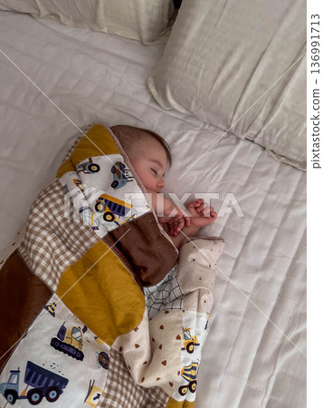 Peaceful sleeping baby under patchwork quilt on white bed Peaceful sleeping baby under patchwork quilt on white bed 136991713