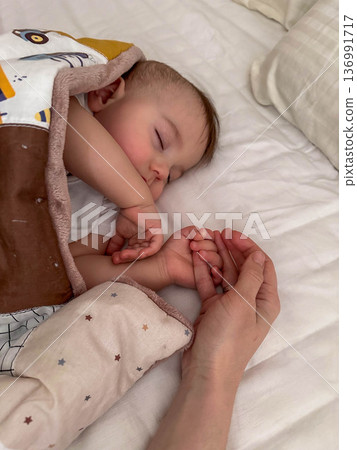 Peaceful sleeping baby holding adult hand Peaceful sleeping baby holding adult hand 136991717