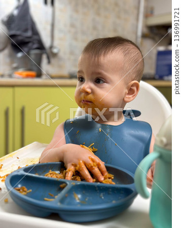 Messy toddler eating pasta in high chair at home 136991721