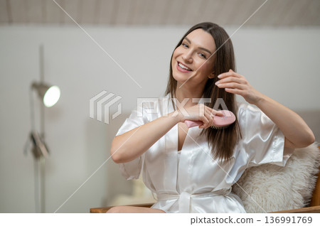Young woman in white brushing her hair and smiling 136991769