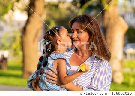Girl kisses mom's cheek in warm sunset glow Girl kisses mom's cheek in warm sunset glow 136992020
