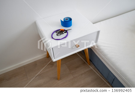 Minimalist bedside table with scissors earplugs mirror and kinesiology tape in bedroom interior Minimalist bedside table with scissors earplugs mirror and kinesiology tape in bedroom interior 136992405