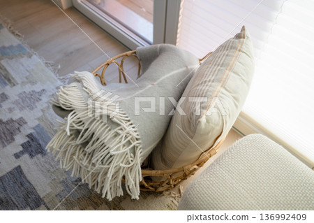 Rattan basket with soft blanket and pillow near window in cozy Scandinavian interior Rattan basket with soft blanket and pillow near window in cozy Scandinavian interior 136992409