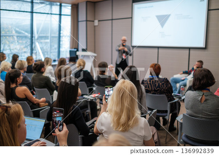 Business conference presentation with engaged audience capturing speaker on smartphones in modern meeting room Business conference presentation with engaged audience capturing speaker on smartphones in modern meeting room 136992839