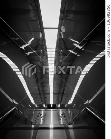 Modern underground station escalator with symmetrical lighting and reflective black and white architecture 136992850