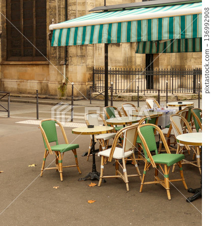 Empty traditional parisian street cafe with chairs and tables under a striped awning, a symbol of european culture and travel Empty traditional parisian street cafe with chairs and tables under a striped awning, a symbol of european culture and travel 136992908