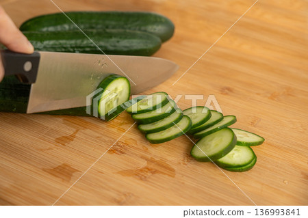 Slicing cucumbers with a large knife on wood cooking board close-up 136993841