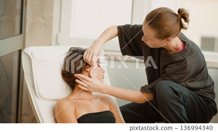 Beauty specialist administers facial and jaw therapy in bright room Beauty specialist administers facial and jaw therapy in bright room 136994340