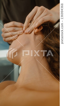 Peaceful woman receives calming ear massage amidst tranquil spa setting Peaceful woman receives calming ear massage amidst tranquil spa setting 136994368