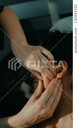 Therapist applying precise finger pressure for ear acupressure treatment 136994382