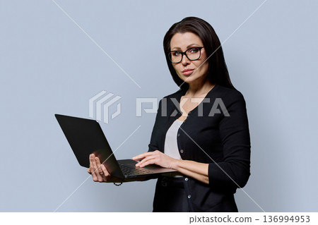 Portrait of mature woman with laptop on grey studio background 136994953