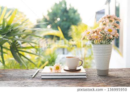 coffee cup and Chrysanthemum flowers in a vase and notebook on wooed table with garden view 136995950