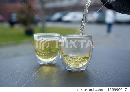 Pouring green tea into a glass from a metal kettle on blurred background, hot drink in teapot 136996647