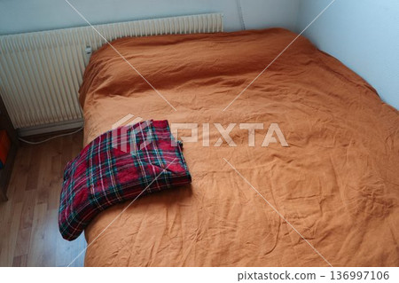 Christmas plaid folded on the side of bed with orange linen. Everyday home scene with seasonal textile and warm color contrast. 136997106