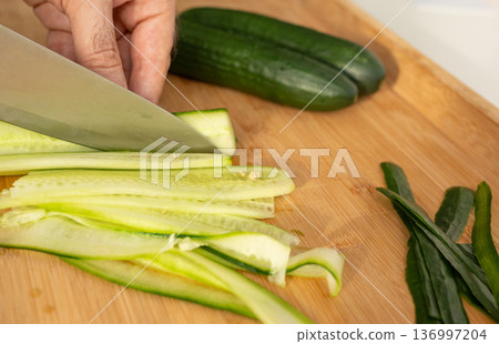 Slicing cucumbers with a large knife on wood cooking board close-up 136997204