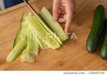 Slicing cucumbers with a large knife on wood cooking board close-up 136997549