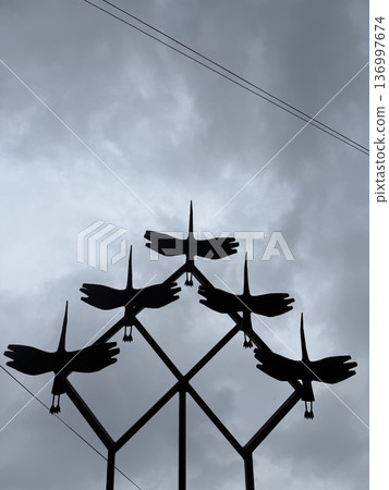 A metal silhouette sculpture of five flying birds against a cloudy gray sky, outdoor public art, freedom concept. 136997674