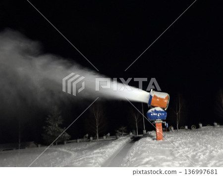 A snow cannon blowing artificial snow on a dark winter night, ski resort maintenance, winter season. A snow cannon blowing artificial snow on a dark winter night, ski resort maintenance, winter season. 136997681