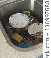 A dirty stainless steel kitchen sink is filled with unwashed pots plates and a sponge, messy home hygiene, daily household chores. 136997688