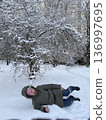 A woman lies happily in deep snow under a frosted tree, winter fun, playful outdoor lifestyle, frosty nature. 136997695